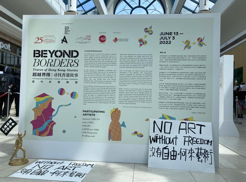 示威者將寫有「沒有自由，何來藝術」標語的紙牌，及反修例運動期間經常出現的「抗爭女神」像，置於「超越界限：尋找香港故事」藝術展展板前。星島記者攝