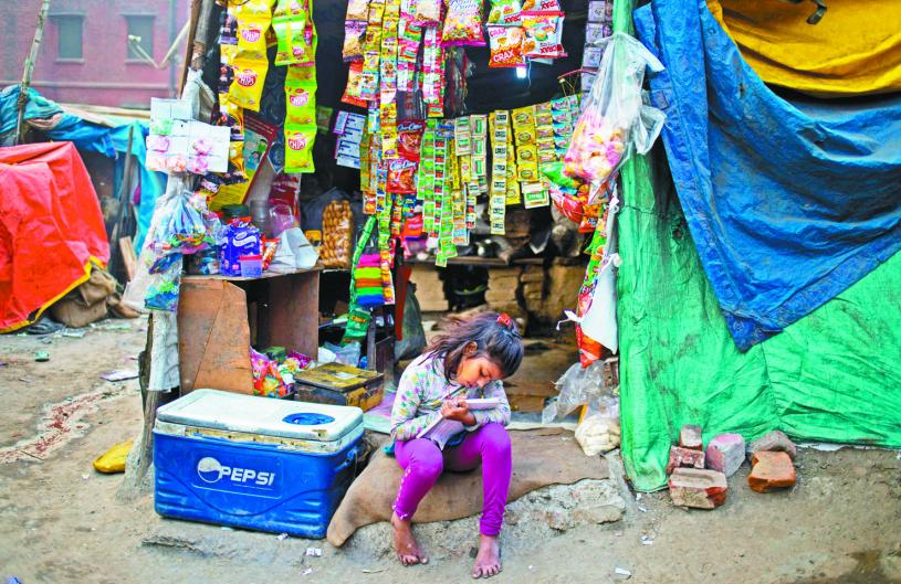 在印度新德里貧民窟，一名印度女孩一邊照看著小賣部，一邊學習。資料圖片