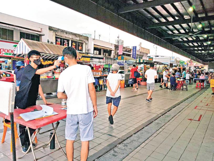 马来西亚防疫严格，到路边的小贩中心吃饭，也得戴口罩、刷手机apps和量体温后，才可用餐。中央社