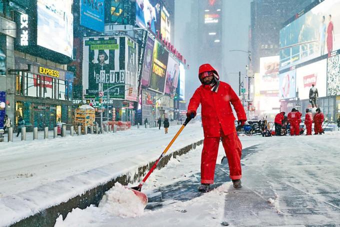 纽约时代广场昨日可见白雪满地，一名工人在铲雪。