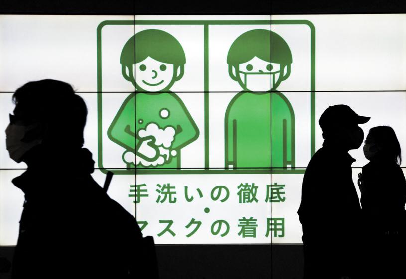 在日本，戴着防护口罩的路人走过显示有关新冠安全措施通知的电子屏幕前。路透社