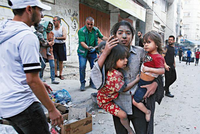 以軍空襲加沙城，巴勒斯坦婦女抱着兩童逃命。
