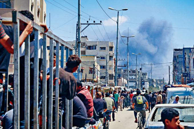 以军空袭加沙南部城镇拉法，人群聚集的街道不远处冒出浓烟。
