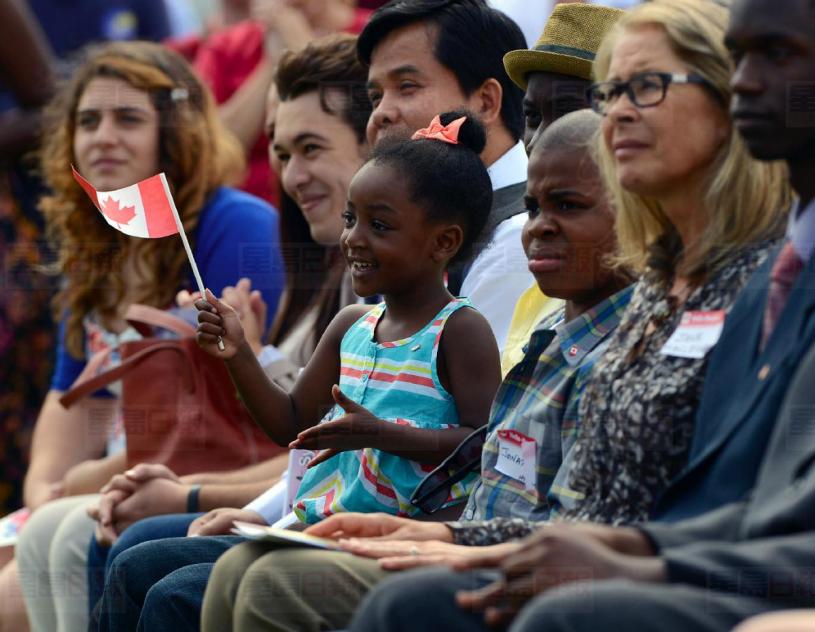 Jasmyne Bowen waves her Canadian flag while sitting on her cousin's lap during the citizenship ceremony for 37 new Canadians at Riverside Park Monday, July 1, 2013. Bowen's uncle, aunt and two cousins were four of the 37 people from 18 different countries who became Canadians during the Canada Day celebration.