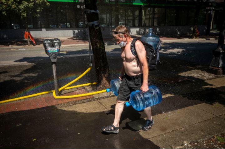 去年6月有一段時間，溫哥華也很炎熱，圖為一個男子兩手各拿著一大樽水，準備在家中飲用。CBC