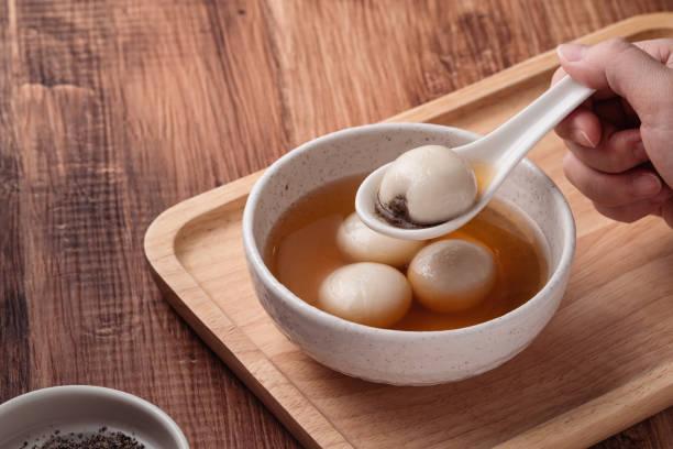 Close up of sesame big tangyuan (tang yuan, glutinous rice dumpling balls) with sweet syrup soup in a bowl on wooden table background for Winter solstice festival food.