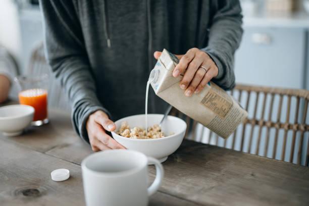 Cropped shot of young Asian mother preparing healthy breakfast, pouring milk over cereals on the kitchen counter. Healthy eating lifestyle