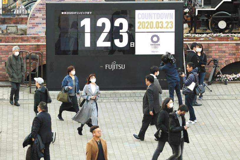  3月23日，行人在日本東京新橋地區經過顯示東京奧運會倒計時的大屏幕。新華社