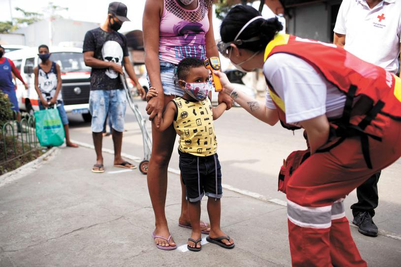巴西里約熱內盧，一名紅十字會成員在批發市場為兒童檢測體溫。美聯社