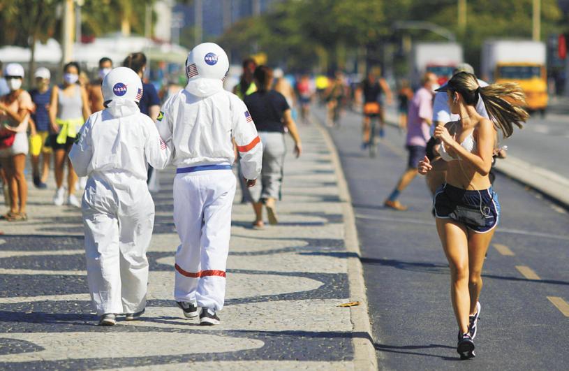 在巴西里約熱內盧，一對夫婦穿著防護「太空服」在海灘旁的人行道上行走。路透社