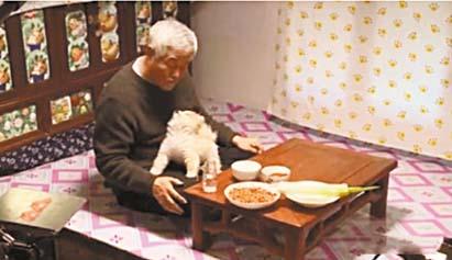 赵本山头发花白，坐炕上与小狗互动。 网上图片