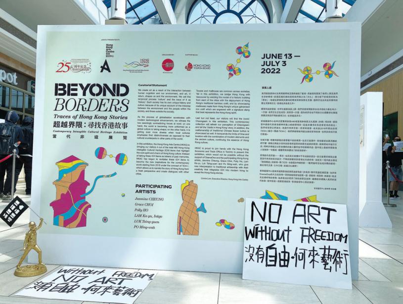■示威者將寫有「沒有自由，何來藝術」標語的紙牌及「香港民主女神」像，置於「超越界限：尋找香港故事」藝術展展板前。
