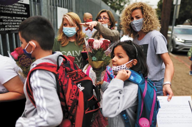 美國疾控中心（CDC）放寬了新冠防疫指南，校園的「檢測留校」政策被取消。圖為去年在洛杉磯格倫代爾，教師在校門口迎接學生返校。路透社資料圖片