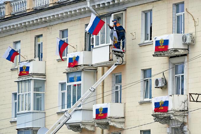 在乌克兰东部卢甘斯克，周二有工人在住宅大厦挂起俄罗斯国旗。