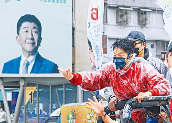國民黨台北市長候選人蔣萬安（紅衣）昨天冒雨拜票。左方為民進黨對手陳時中的巨型宣傳板。

